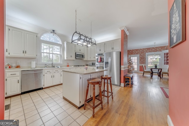 kitchen featuring white cabinetry, a kitchen breakfast bar, decorative light fixtures, a kitchen island, and appliances with stainless steel finishes