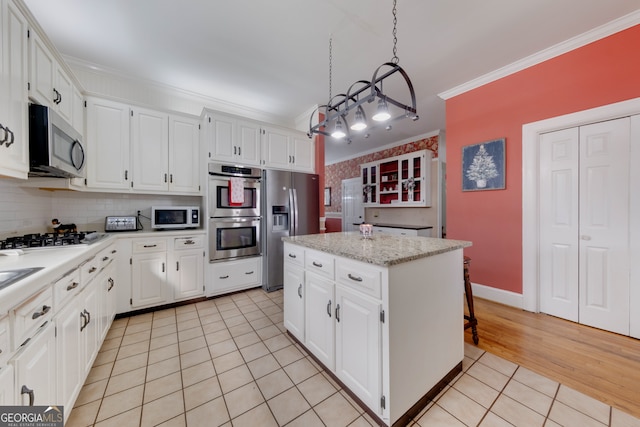 kitchen with pendant lighting, crown molding, appliances with stainless steel finishes, a kitchen island, and white cabinetry