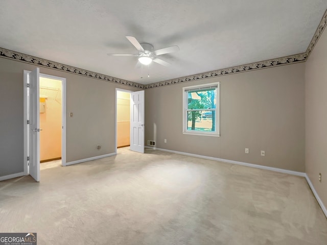 interior space with a walk in closet, light colored carpet, and ceiling fan