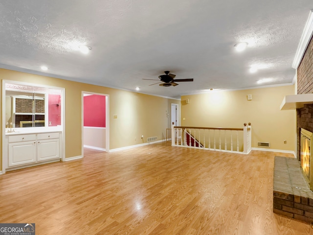 unfurnished living room with light wood-type flooring, a brick fireplace, ceiling fan, and ornamental molding