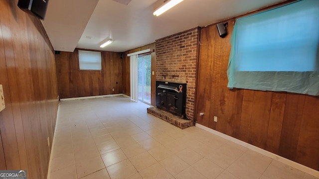 unfurnished living room featuring a wood stove, wooden walls, and brick wall