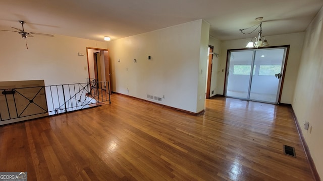 empty room with ceiling fan with notable chandelier and wood-type flooring