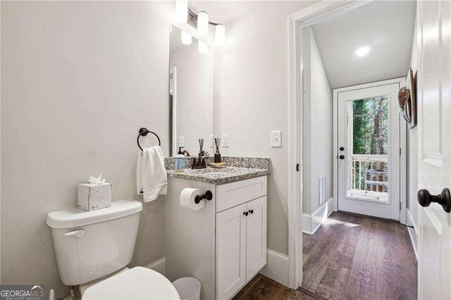 bathroom with toilet, vanity, lofted ceiling, and hardwood / wood-style flooring