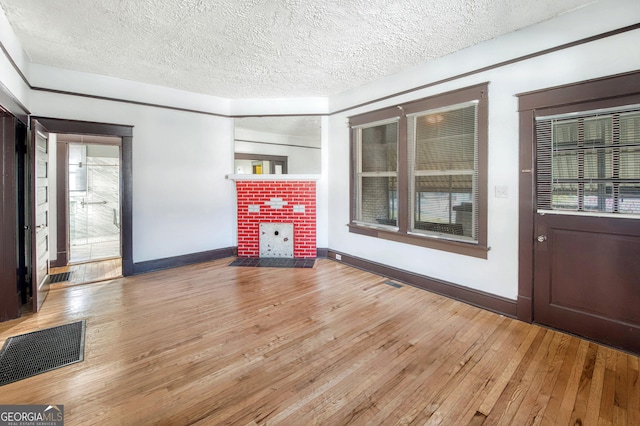 unfurnished living room featuring hardwood / wood-style floors, a textured ceiling, and a brick fireplace