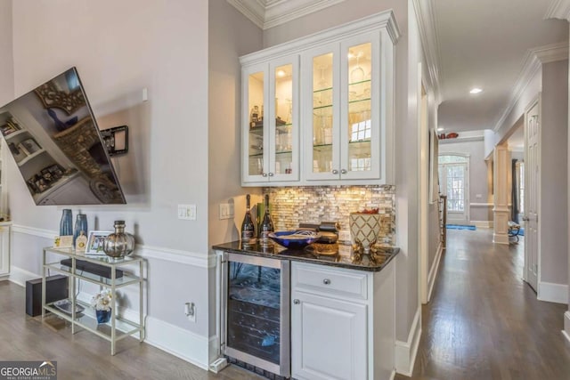 bar featuring wine cooler, ornamental molding, hardwood / wood-style flooring, dark stone countertops, and white cabinetry