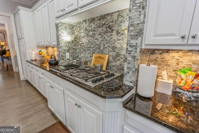 kitchen with white cabinets, dark stone countertops, tasteful backsplash, light hardwood / wood-style floors, and stainless steel gas cooktop