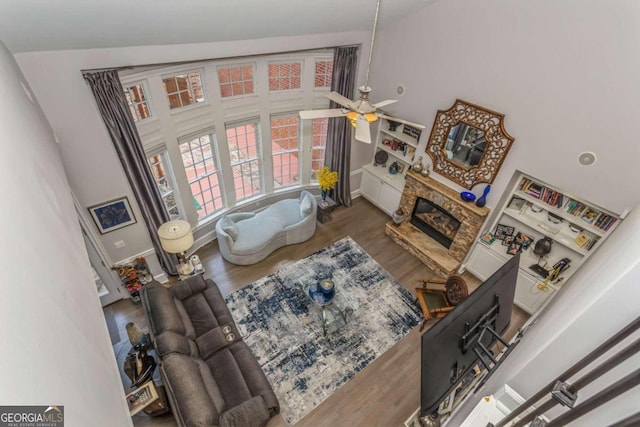 living room with wood-type flooring, high vaulted ceiling, a stone fireplace, and ceiling fan