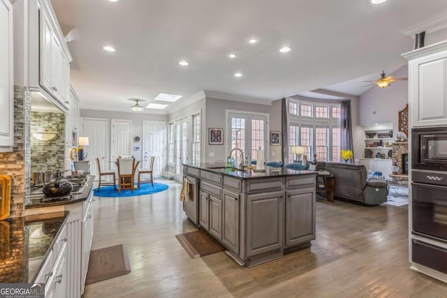 kitchen featuring sink, a center island with sink, hardwood / wood-style flooring, white cabinets, and a stone fireplace