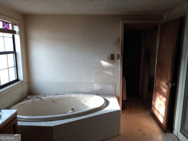 bathroom with a relaxing tiled tub, vanity, a textured ceiling, and a wealth of natural light