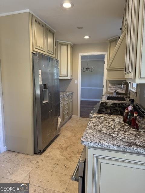 kitchen with light stone countertops, sink, a notable chandelier, cream cabinets, and refrigerator