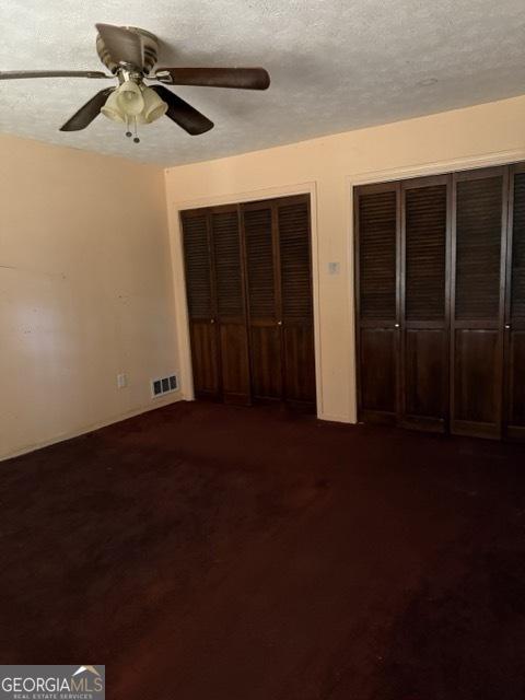 unfurnished bedroom with dark colored carpet, ceiling fan, and a textured ceiling