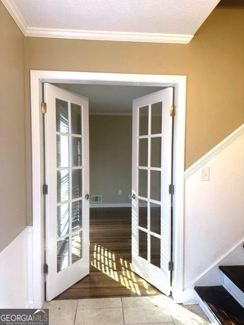 entryway with french doors, a textured ceiling, light hardwood / wood-style floors, and ornamental molding