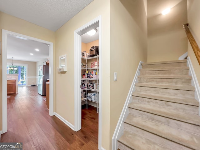 stairs featuring wood-type flooring, a textured ceiling, and an inviting chandelier