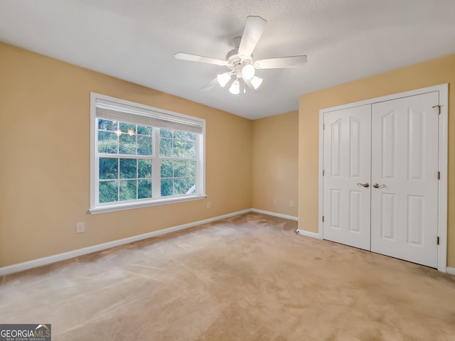 unfurnished bedroom featuring ceiling fan, light colored carpet, a textured ceiling, and a closet