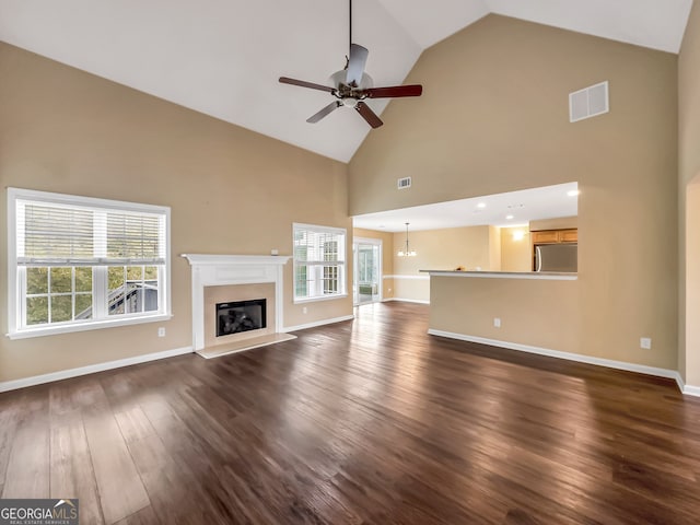 unfurnished living room with ceiling fan with notable chandelier, dark hardwood / wood-style flooring, high vaulted ceiling, and a healthy amount of sunlight