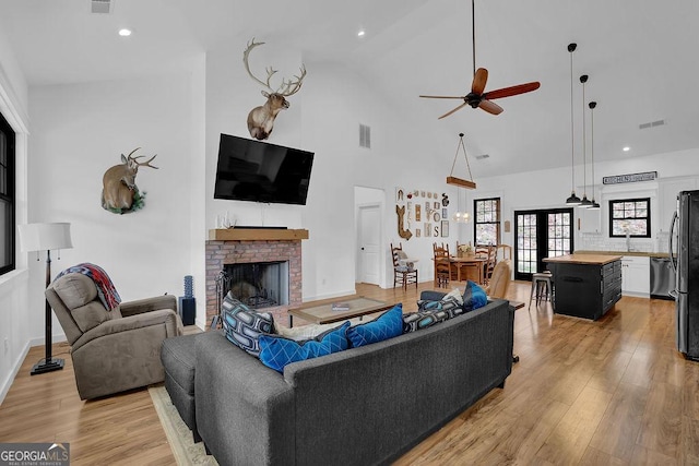 living room featuring ceiling fan, a brick fireplace, high vaulted ceiling, and light hardwood / wood-style floors