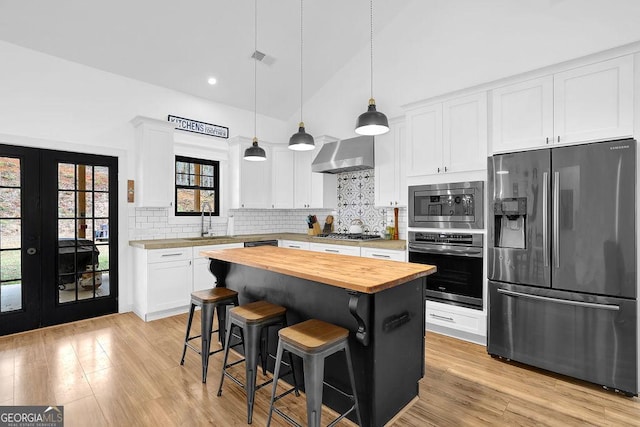 kitchen with white cabinetry, wall chimney range hood, butcher block countertops, and appliances with stainless steel finishes