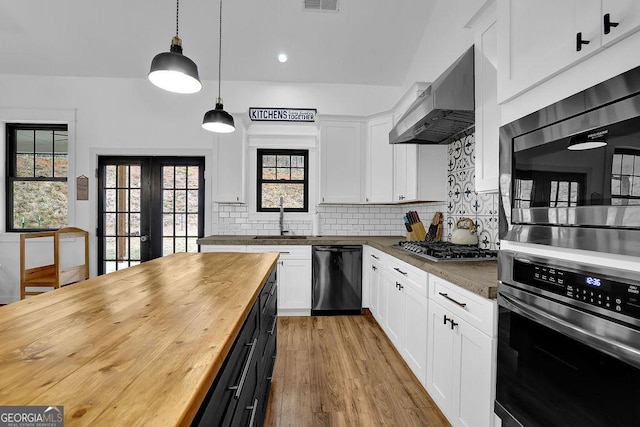 kitchen featuring butcher block counters, extractor fan, decorative light fixtures, appliances with stainless steel finishes, and white cabinets