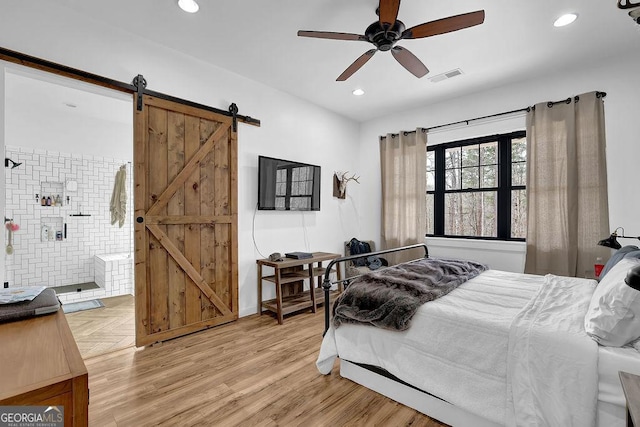 bedroom with ensuite bath, a barn door, and ceiling fan