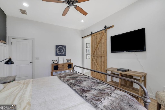 bedroom with a barn door, hardwood / wood-style floors, and ceiling fan