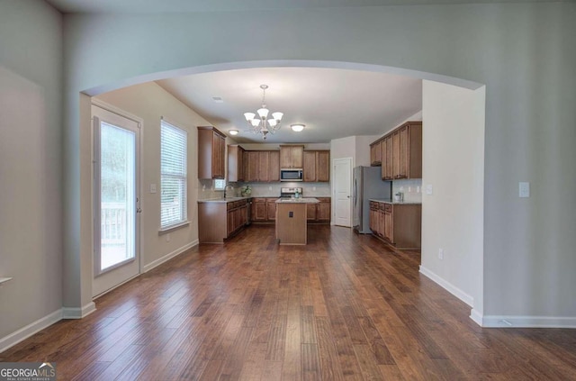 kitchen with appliances with stainless steel finishes, backsplash, dark wood-type flooring, pendant lighting, and a center island