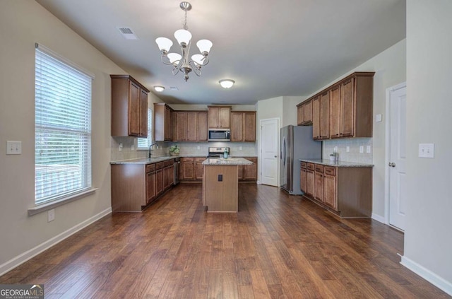 kitchen with decorative backsplash, dark hardwood / wood-style flooring, stainless steel appliances, decorative light fixtures, and a center island