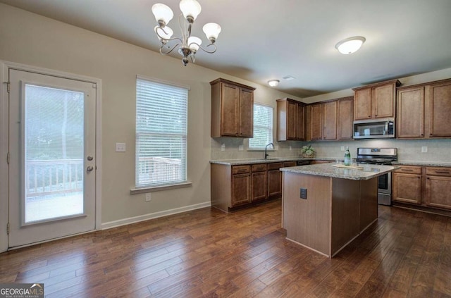 kitchen with a center island, backsplash, dark wood-type flooring, appliances with stainless steel finishes, and decorative light fixtures