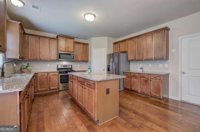 kitchen with sink, dark wood-type flooring, decorative backsplash, a kitchen island, and appliances with stainless steel finishes