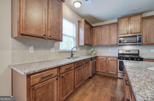 kitchen with light stone countertops, appliances with stainless steel finishes, dark hardwood / wood-style flooring, tasteful backsplash, and sink