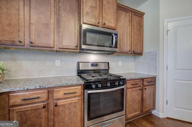 kitchen with decorative backsplash, light stone counters, dark hardwood / wood-style flooring, and stainless steel appliances