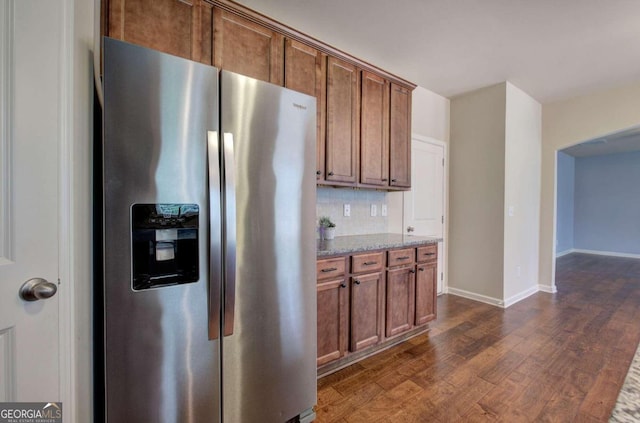 kitchen featuring decorative backsplash, stainless steel fridge with ice dispenser, dark wood-type flooring, and light stone counters