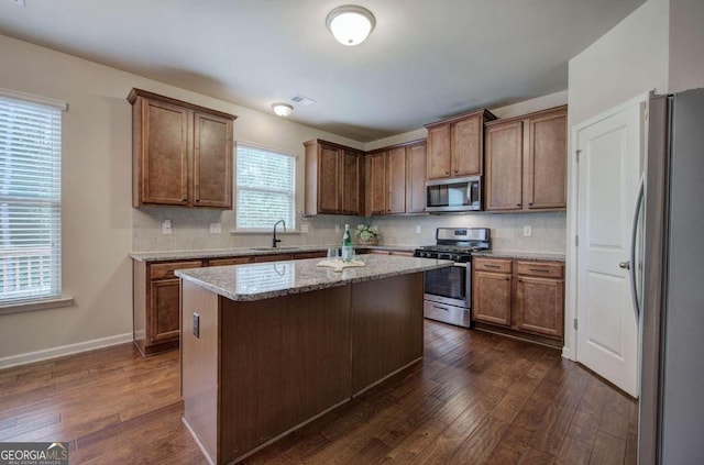 kitchen featuring a center island, tasteful backsplash, light stone counters, dark hardwood / wood-style floors, and appliances with stainless steel finishes