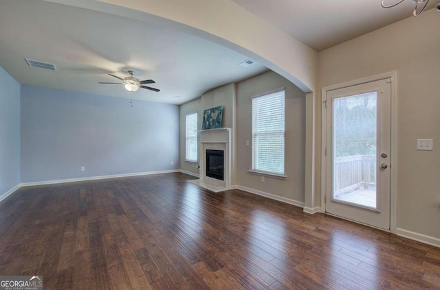 unfurnished living room featuring ceiling fan, a healthy amount of sunlight, and dark wood-type flooring