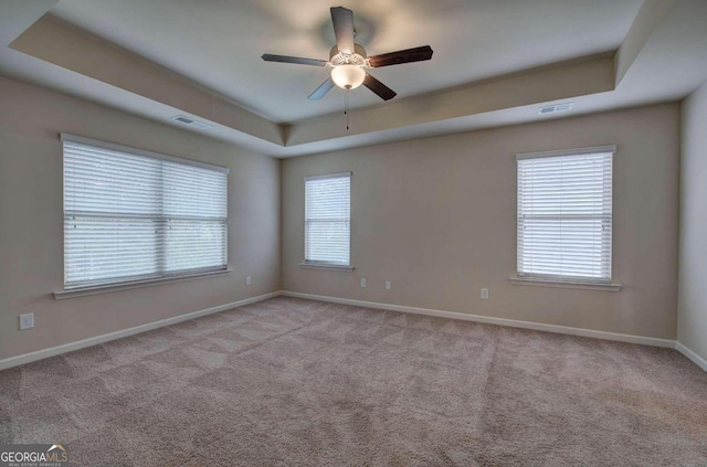 carpeted spare room with ceiling fan, a wealth of natural light, and a tray ceiling