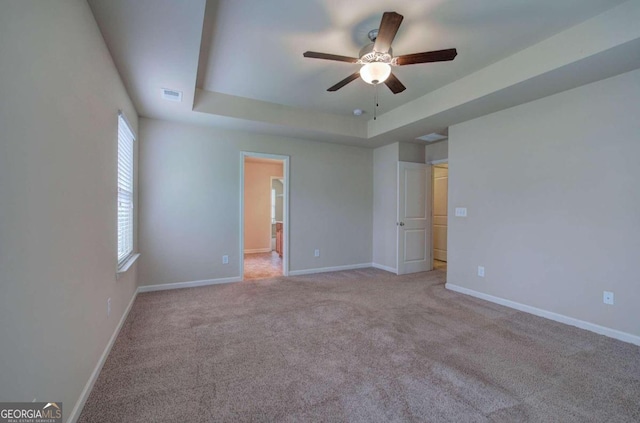 unfurnished room with a raised ceiling, ceiling fan, and light colored carpet