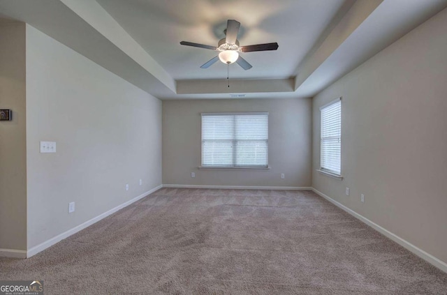 carpeted spare room featuring a raised ceiling and ceiling fan