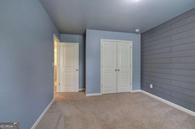 unfurnished bedroom featuring light colored carpet, wooden walls, and a closet