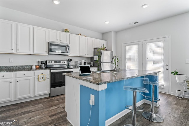 kitchen featuring white cabinets, stainless steel appliances, dark wood-type flooring, and an island with sink