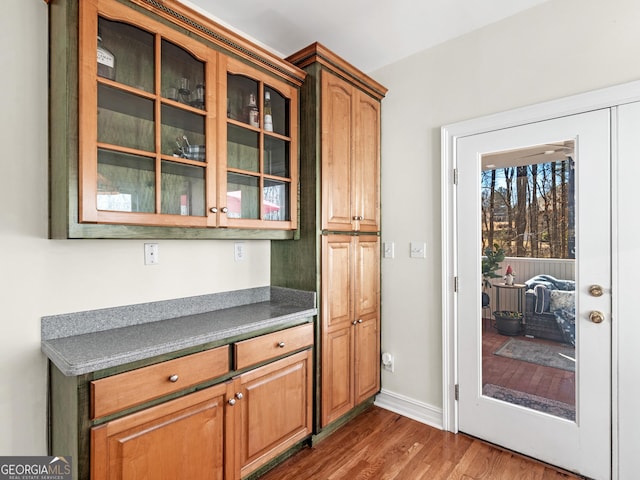 kitchen with dark countertops, wood finished floors, glass insert cabinets, and baseboards