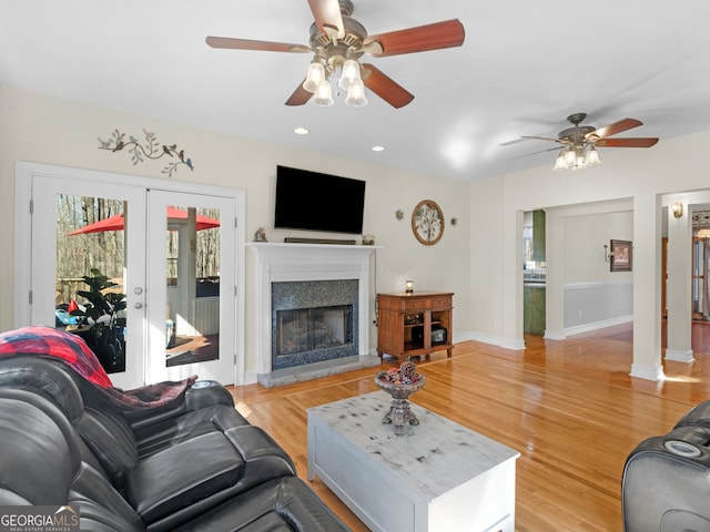 living area with baseboards, a fireplace with raised hearth, french doors, light wood-style floors, and recessed lighting