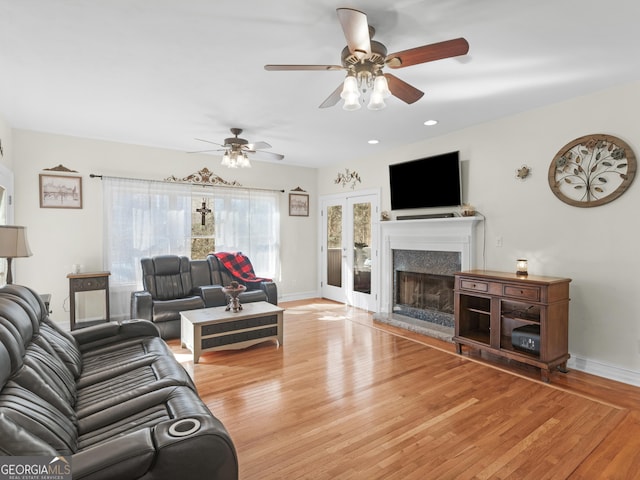 living room with baseboards, a fireplace with raised hearth, ceiling fan, and light wood finished floors