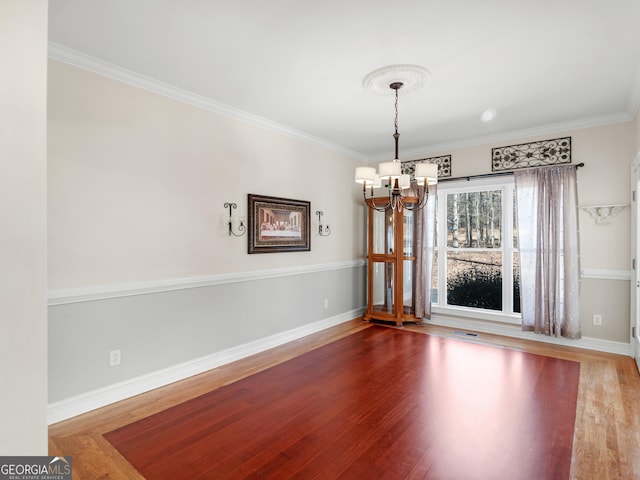 unfurnished dining area with hardwood / wood-style flooring, ornamental molding, and a notable chandelier