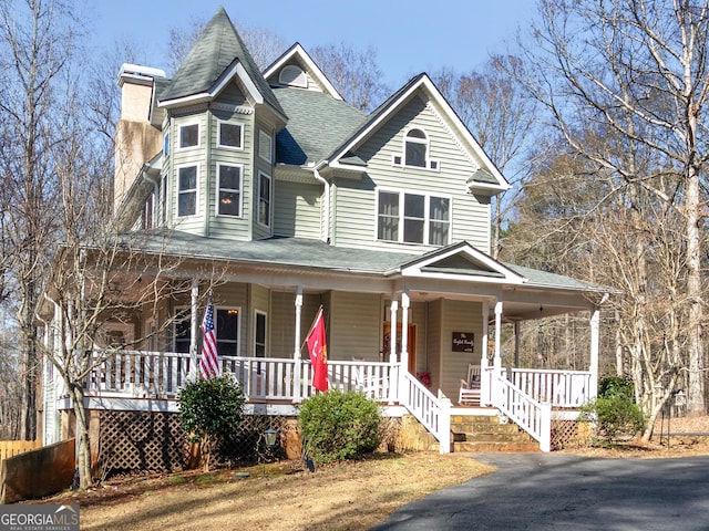 victorian-style house featuring a shingled roof, a chimney, and a porch