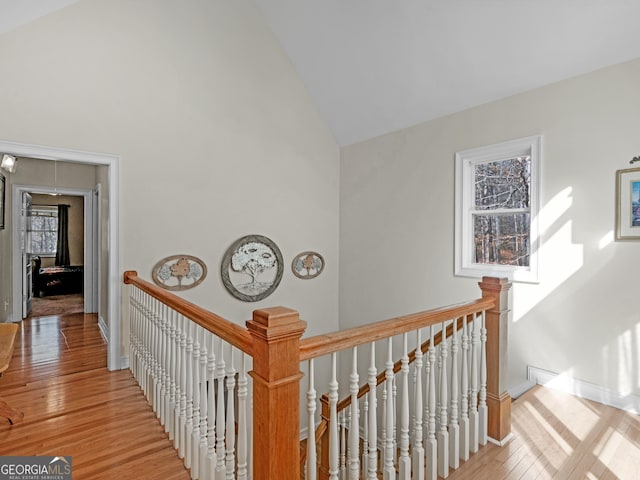 corridor with high vaulted ceiling and light hardwood / wood-style flooring