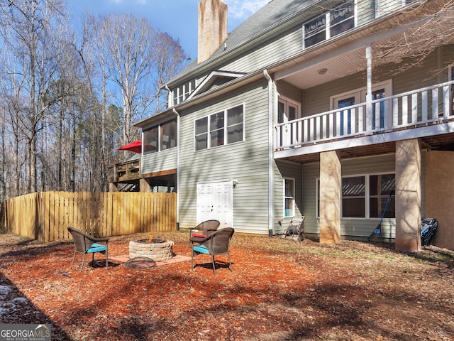 rear view of house with a balcony, a chimney, fence, and a fire pit