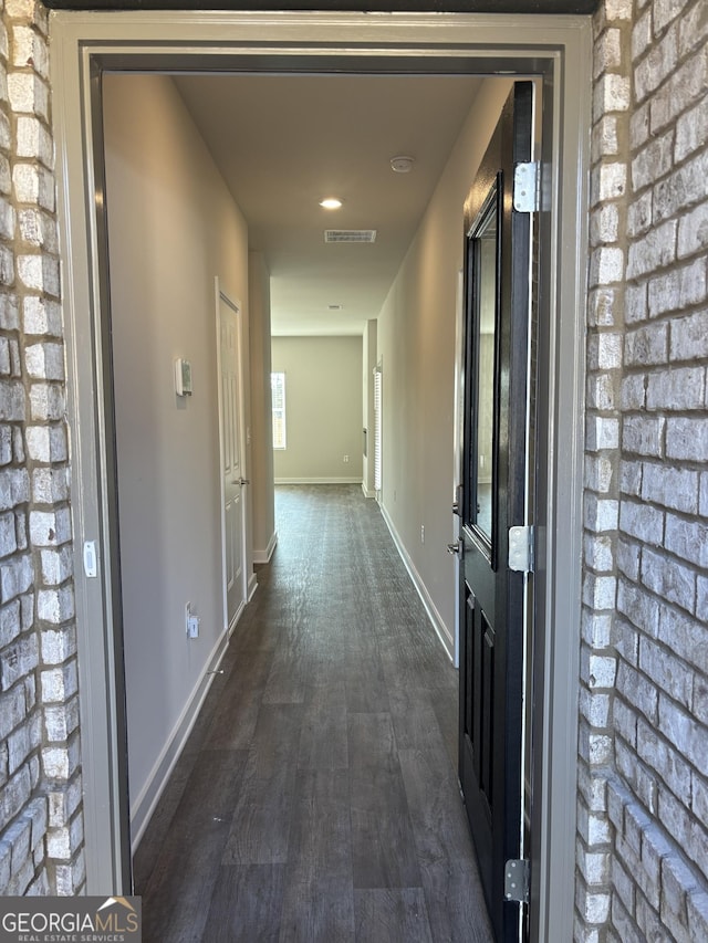 corridor with brick wall and dark hardwood / wood-style flooring