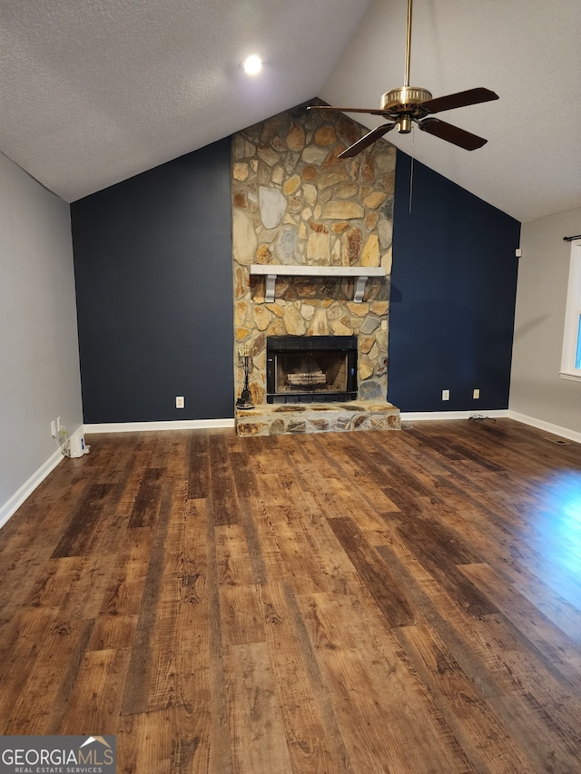 unfurnished living room with a textured ceiling, ceiling fan, hardwood / wood-style floors, a stone fireplace, and lofted ceiling