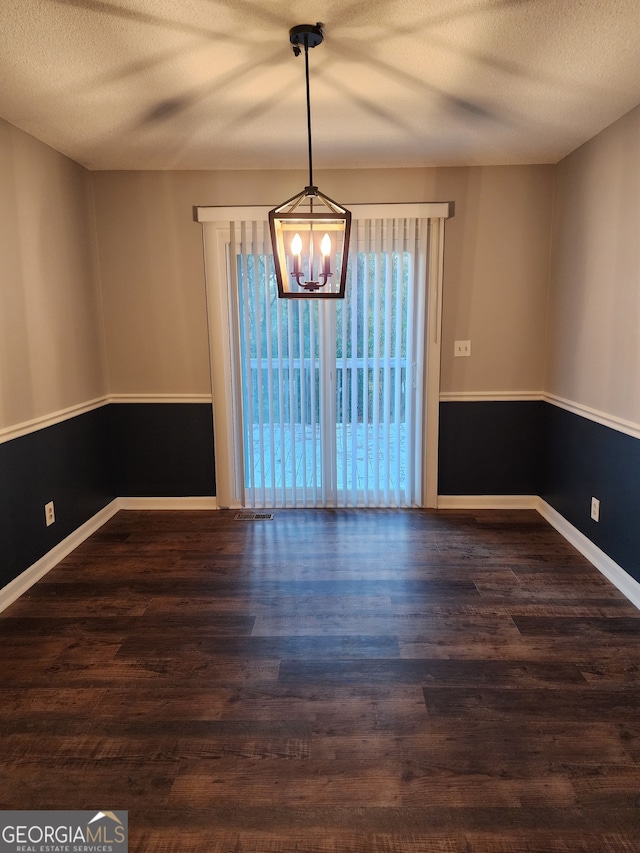 unfurnished dining area with a textured ceiling, dark wood-type flooring, and a chandelier