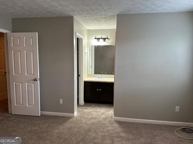 unfurnished bedroom with connected bathroom, sink, light colored carpet, and a textured ceiling