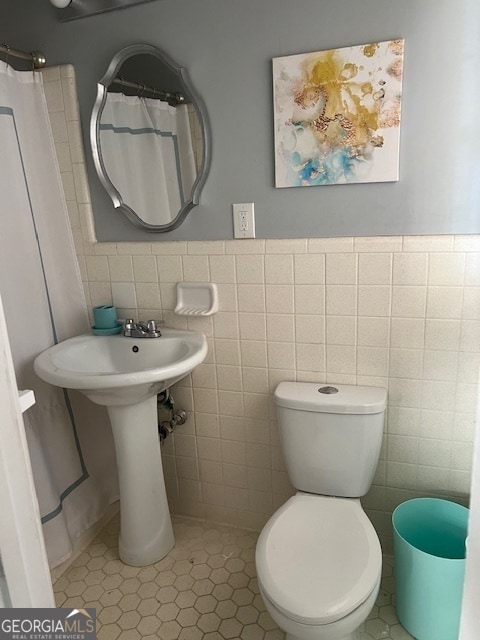 bathroom featuring tile patterned flooring, a shower with shower curtain, toilet, and tile walls